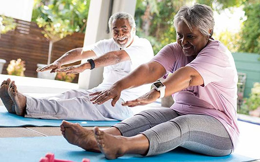 Older couple sitting on their yoga mat, trying to touch their feet
