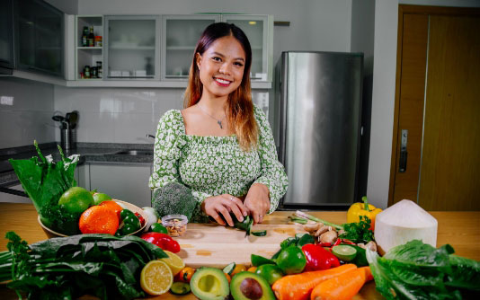 A woman stands at a cutting board chopping vegetables