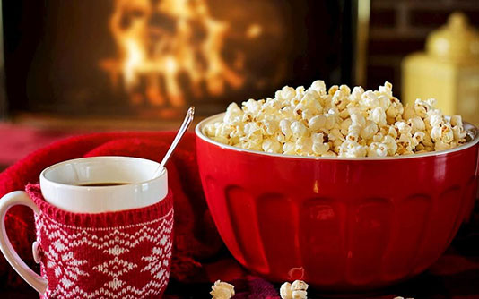 A mug and popcorn in a red bowl in front of a fire