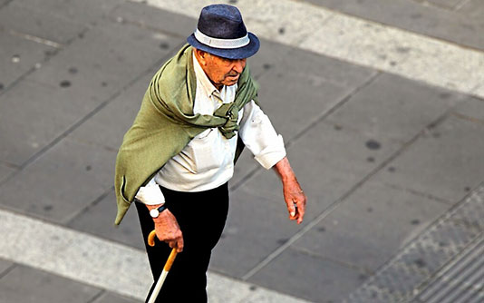 Old man crossing a road holding a cane