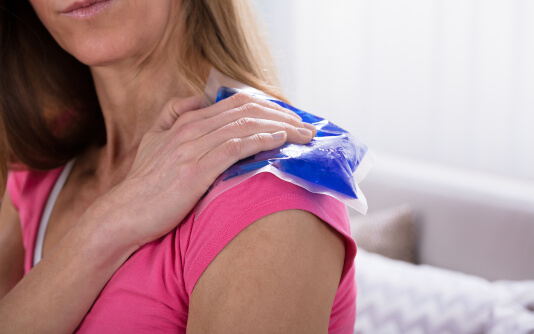 A woman holds an ice pack on her shoulder.