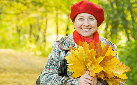Woman with a red hat, outside in the forest holding a bouquet of orange leaves in fall