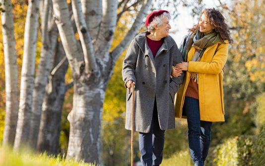 Woman walking with elderly woman with cane in the fall season