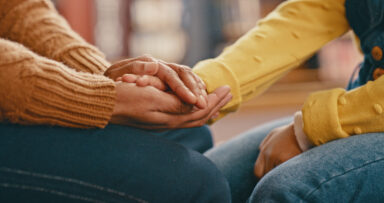 Close up of two people with medium skin holding hands, indicating that one person is offering support to the other. Gros plan sur deux personnes &agrave; la peau moyennement fonc&eacute;e se tenant la main, sugg&eacute;rant que l&rsquo;une apporte son soutien &agrave; l&rsquo;autre.