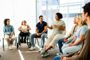 A group of people with varying skin tones sitting in a circle, participating in a group therapy session. Un groupe de personnes aux teints de peau vari&eacute;s, assises en cercle, participant &agrave; une s&eacute;ance de th&eacute;rapie de groupe.
