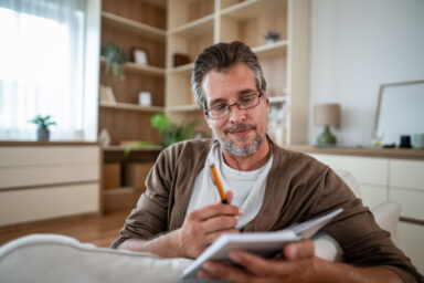 A person with light skin sitting on a couch, holding a pen and notebook. Une personne &agrave; la peau claire assise sur un canap&eacute;, tenant un stylo et un cahier. 